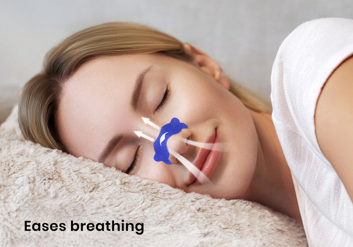 Close-up of a smiling woman sleeping on a plush pillow with a blue nasal strip on her nose and airflow graphics. Text overlay: "Eases breathing".