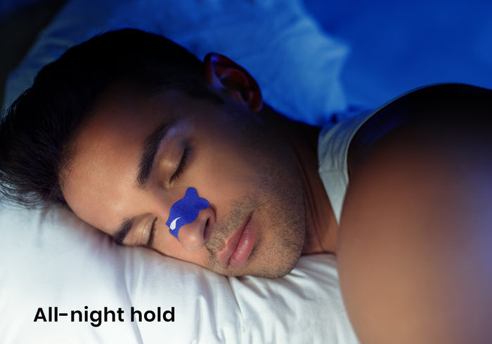 Close-up of a man sleeping with a blue Manta nasal strip on his nose under blue lighting. Text overlay: "All-night hold".